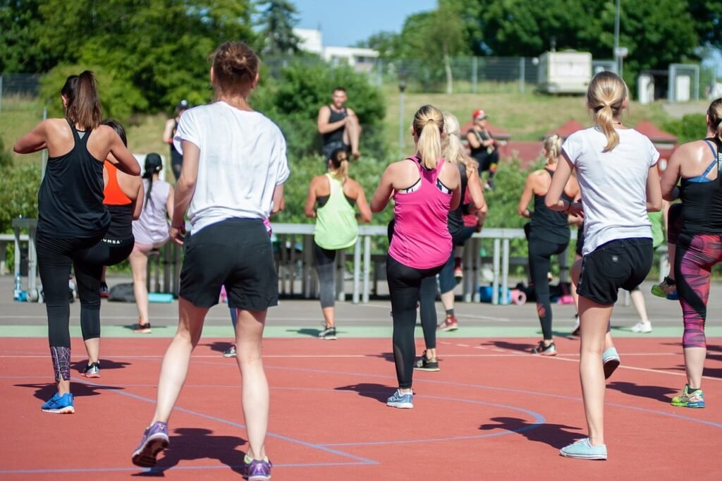 Grupo de personas participando en una clase de ejercicio al aire libre en una pista deportiva, siguiendo las indicaciones del instructor